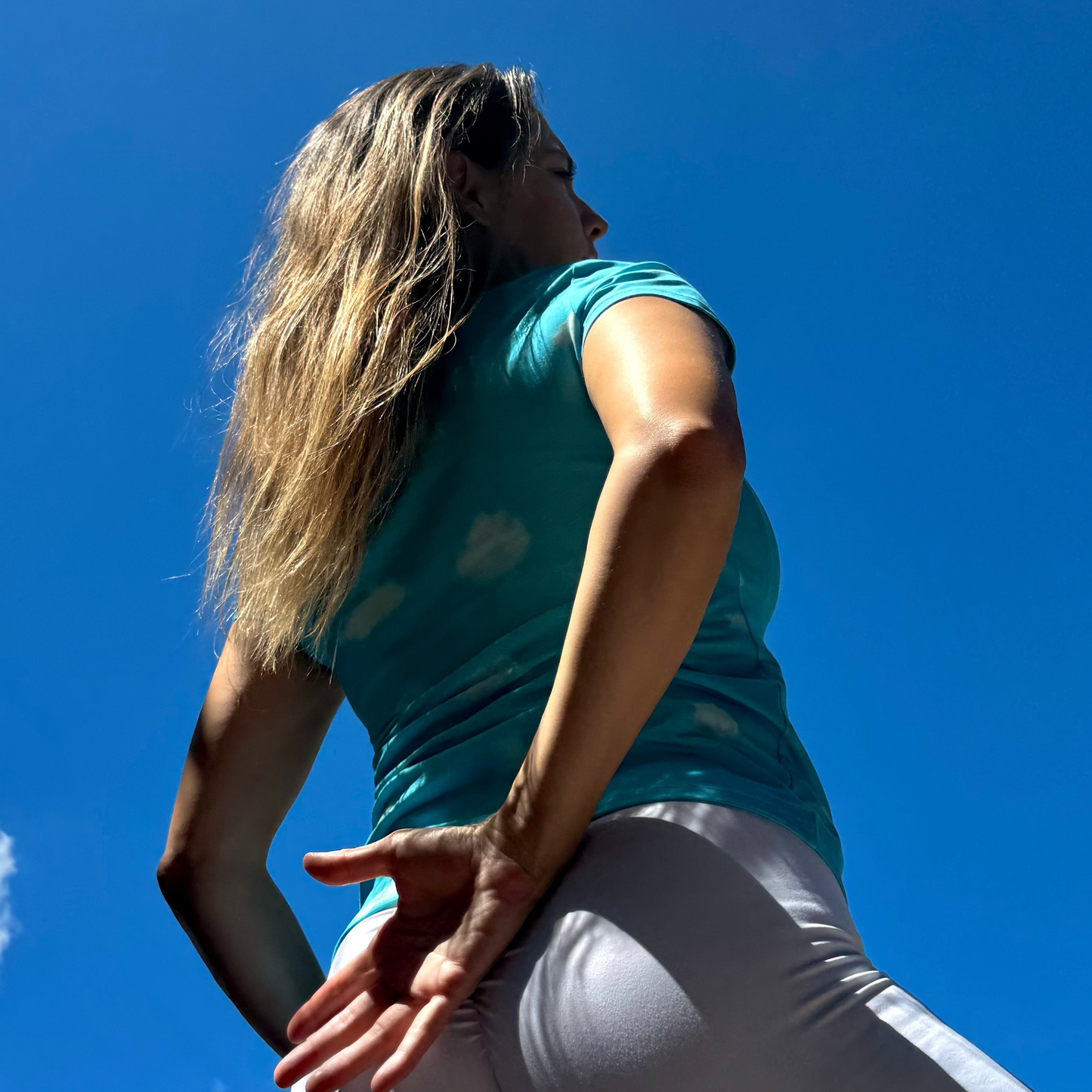 Woman in a blue cloud shirt and white pants against a clear blue sky.