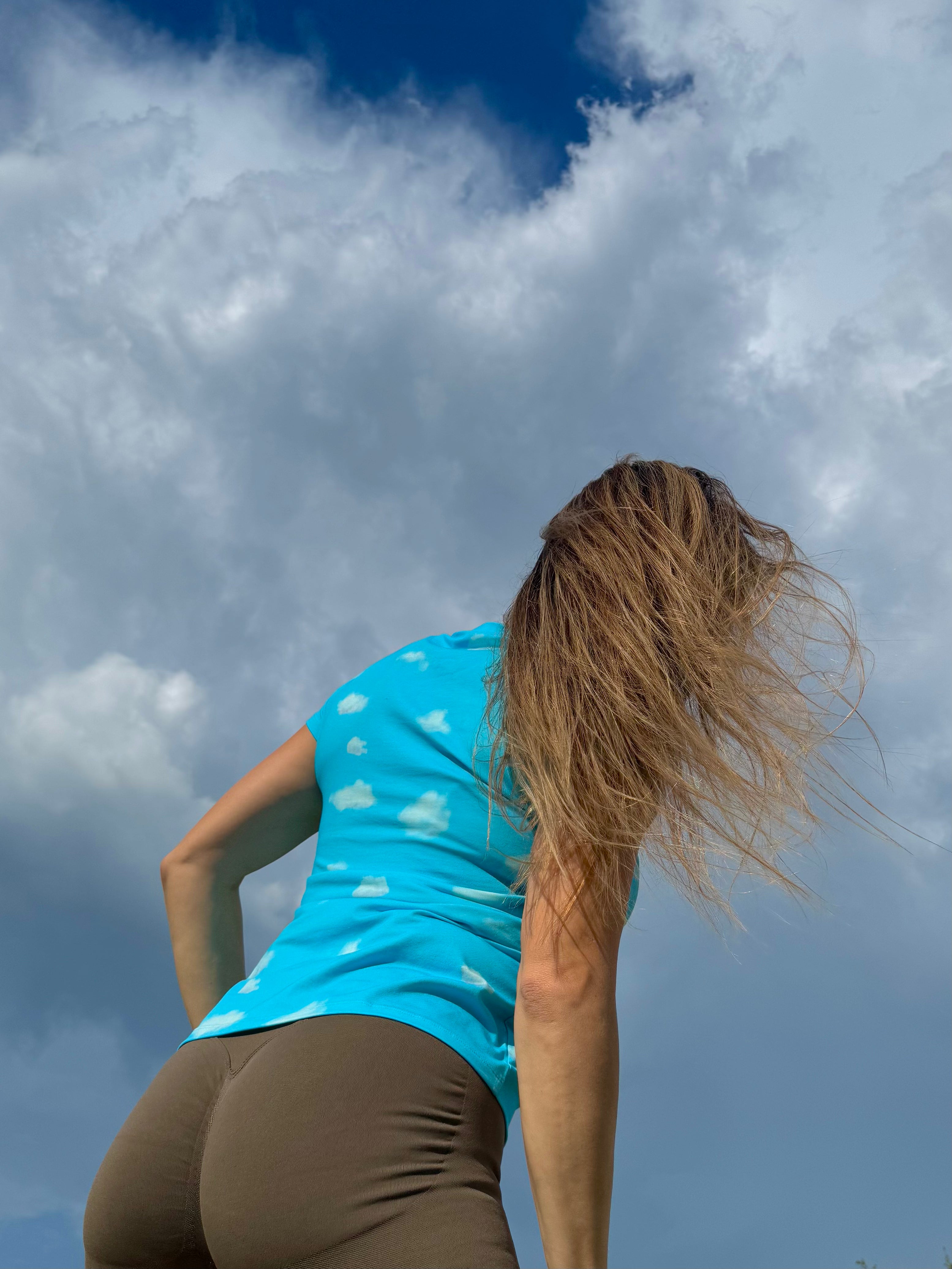 Person wearing Relax with Me tee with cloud patterns against a blue sky