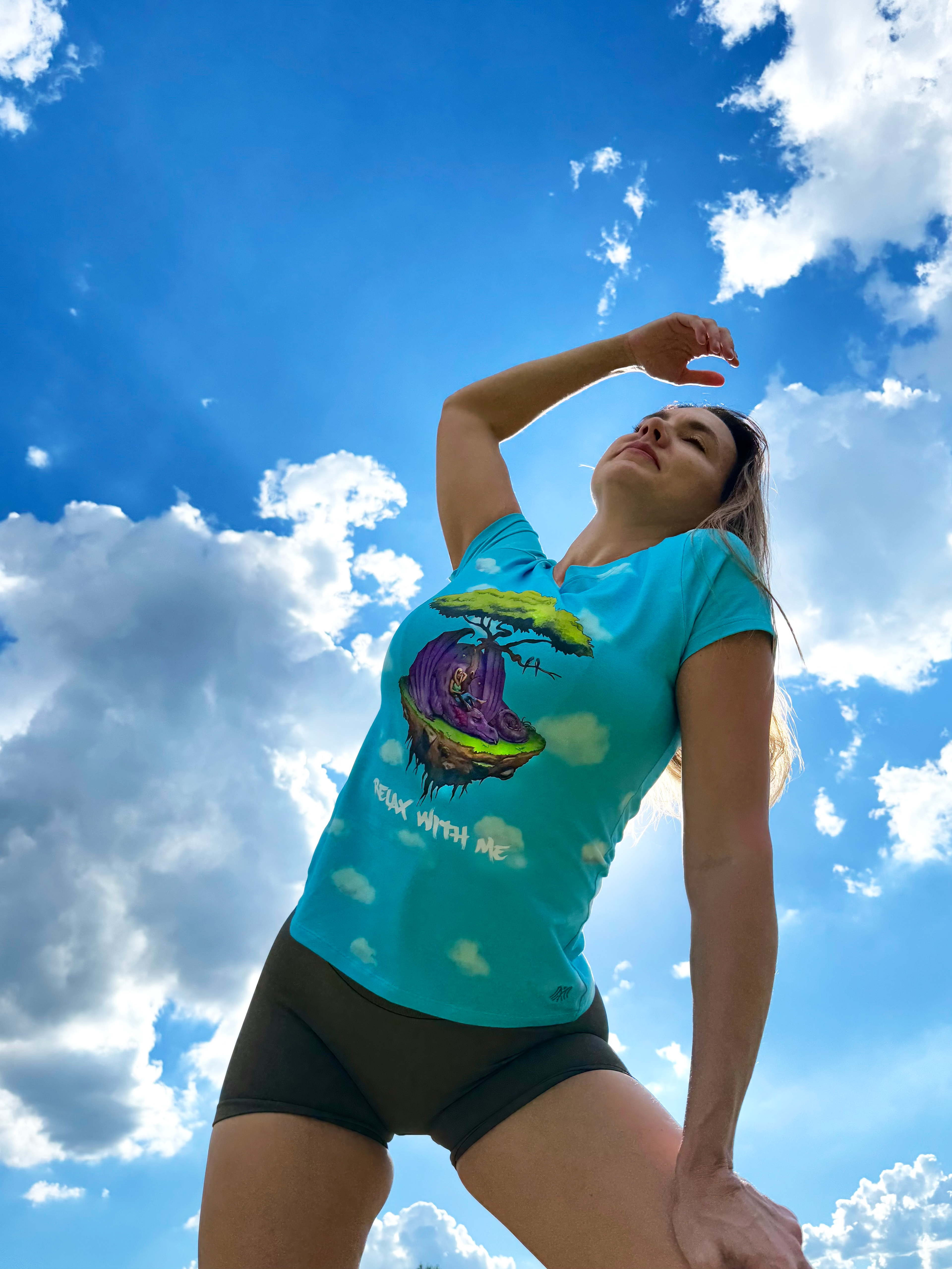 Person wearing a turquoise t-shirt with a graphic design against a blue sky with clouds